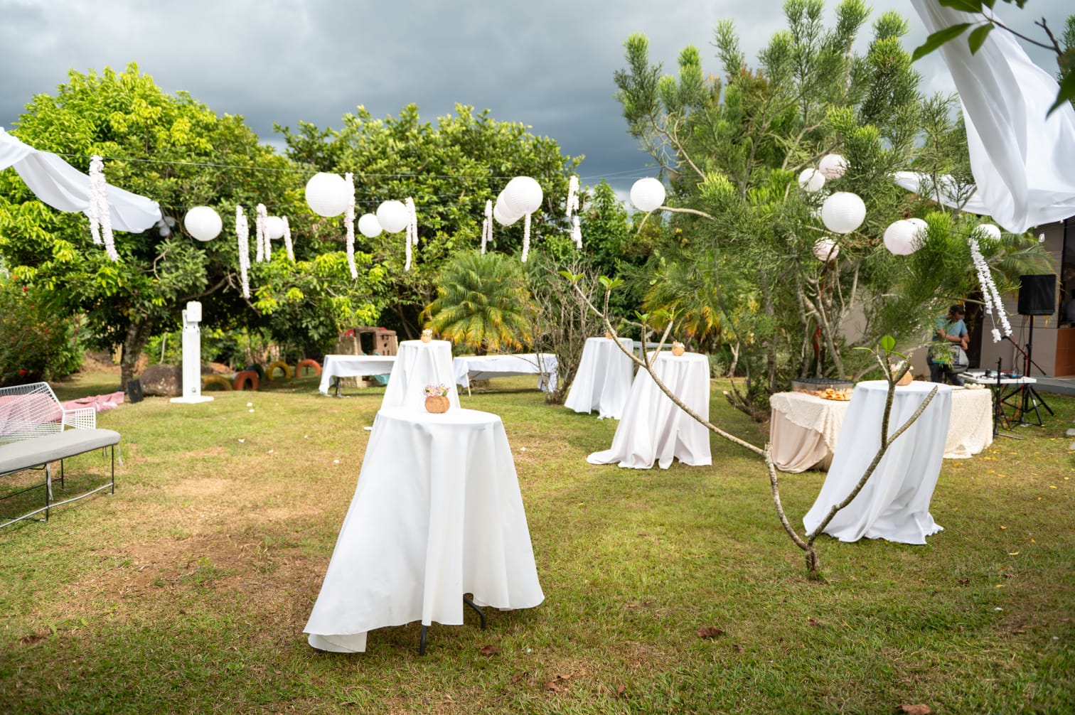 Cóctel al aire libre con mesas altas y lámparas blancas